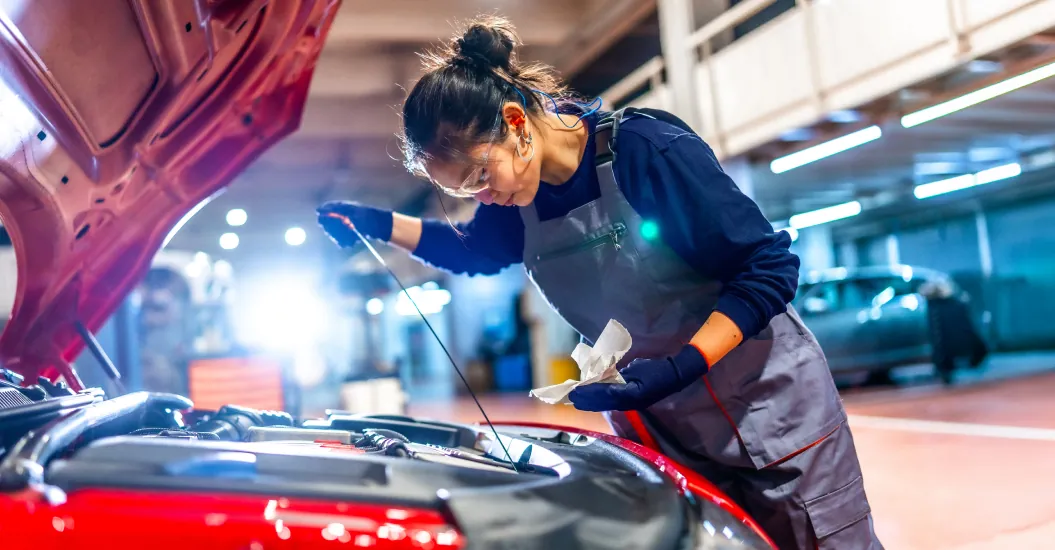A female car mechanic checking under the hood of a red car in a service garage.