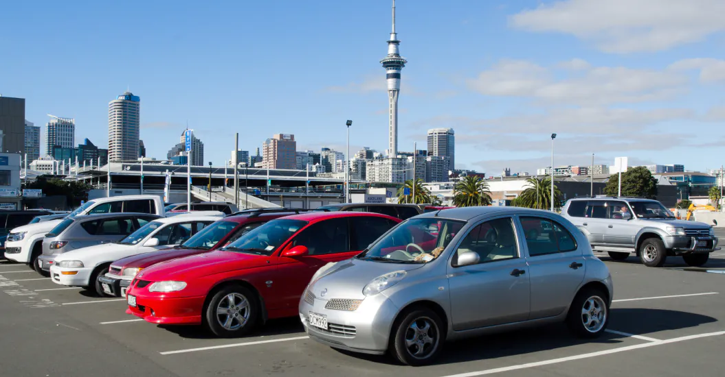 Cars parked in an open-air Auckland car park, with the city skyline and Sky Tower in the background.
