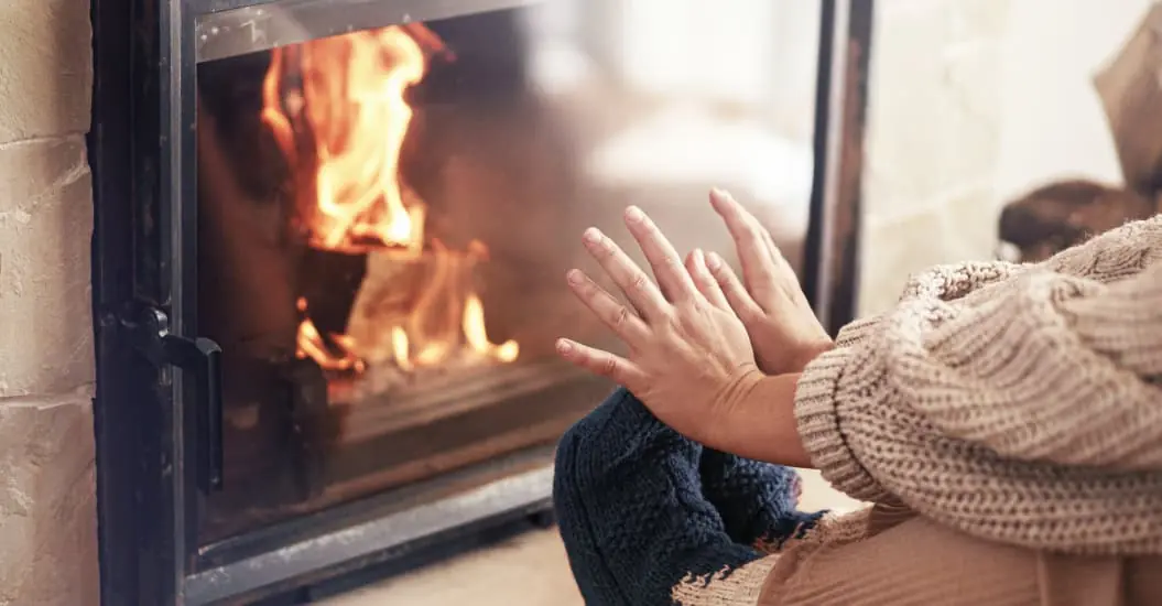 Woman warming up hands and feet next to fireplace