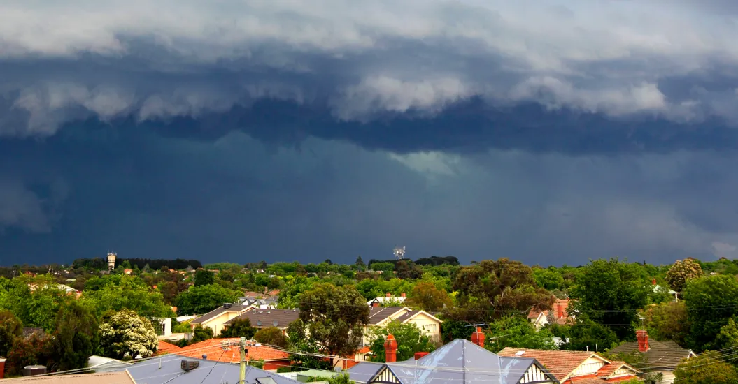 Suburban New Zealand neighbourhood with houses and tress under dramatic storm clouds