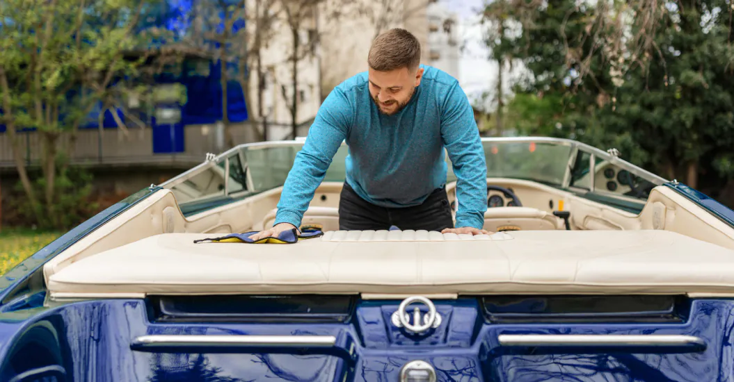 A man in a teal long-sleeve shirt is cleaning the interior seating area of a blue boat parked outside
